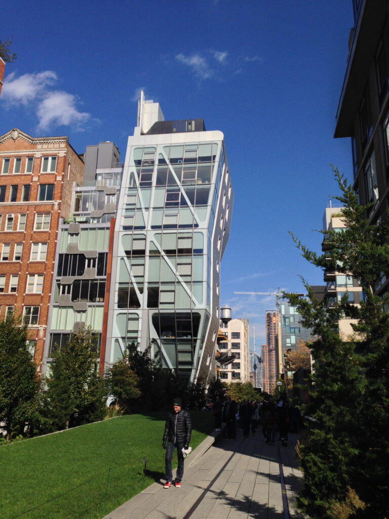 A large building featuring a prominent tall glass window, reflecting the surrounding environment in its sleek surface along the side of the highland, an elevated walkway passing between buildings 